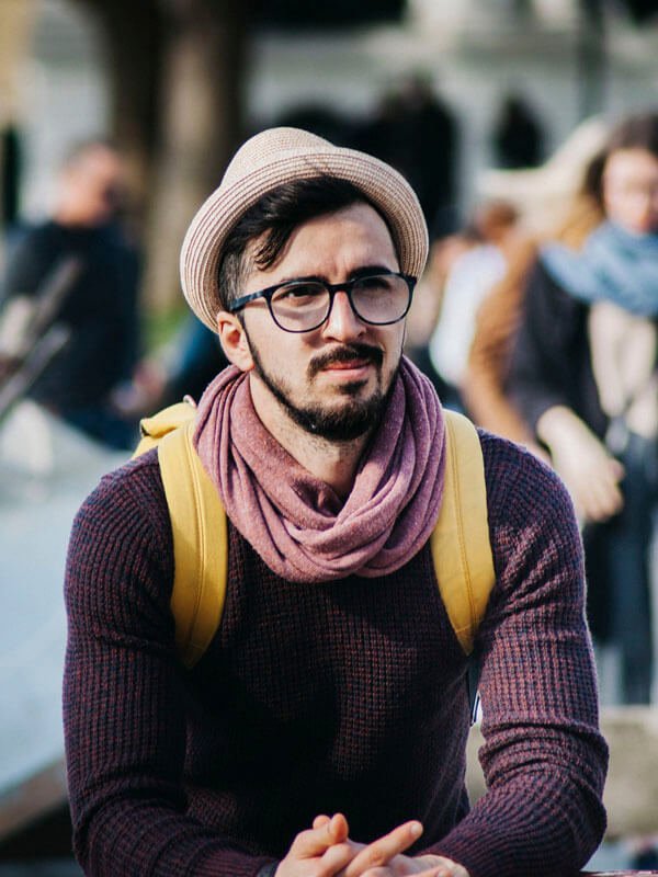 Smiling student with a hat and backpack in a busy city street