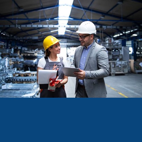 Two business managers in hard hats with tablets inside a factory